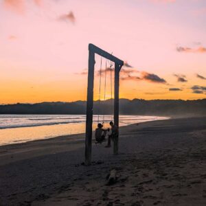 People on swings at sunset on a beach
